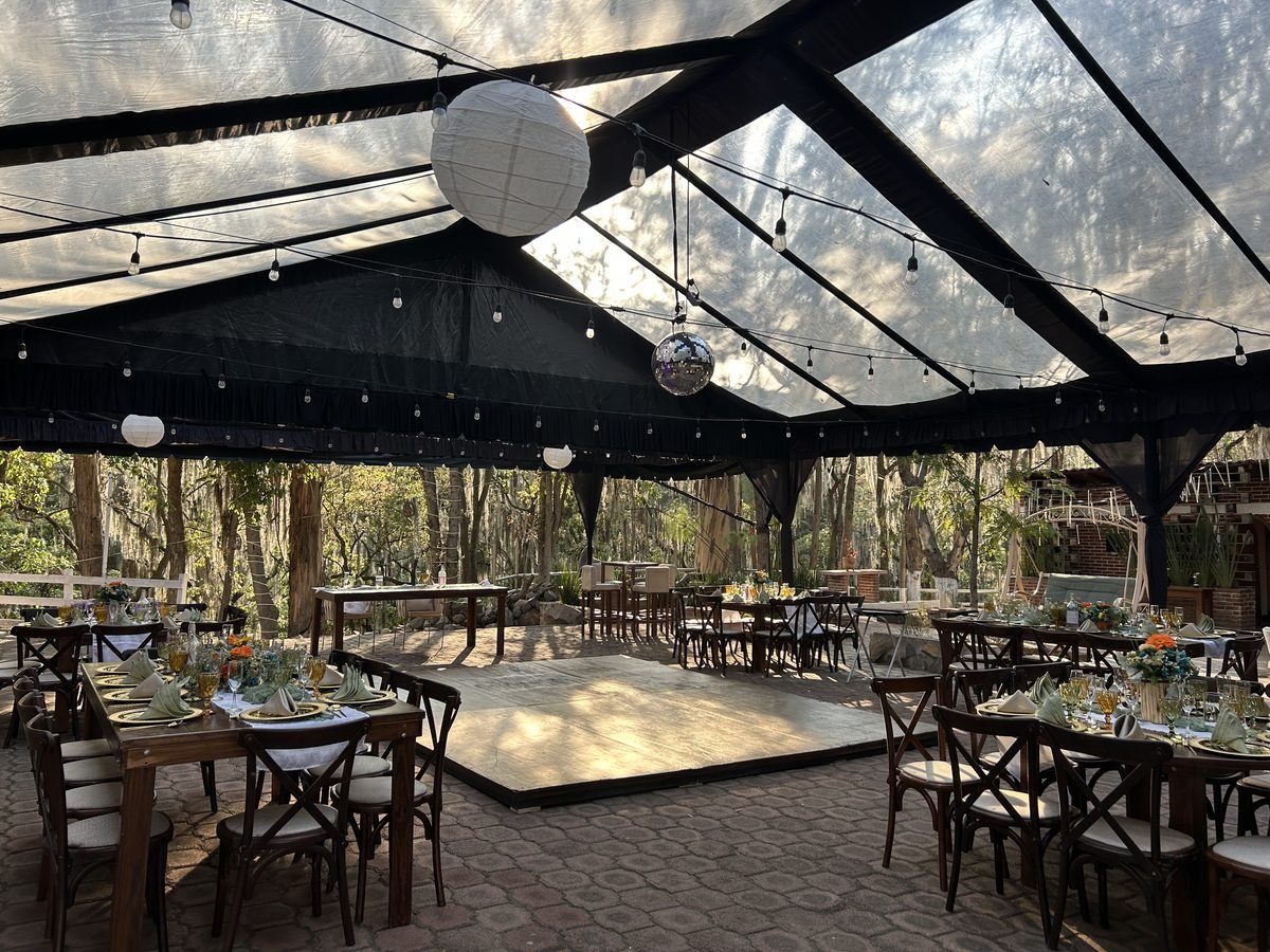 Carpa con pista de baile y mesas decoradas, entre los árboles